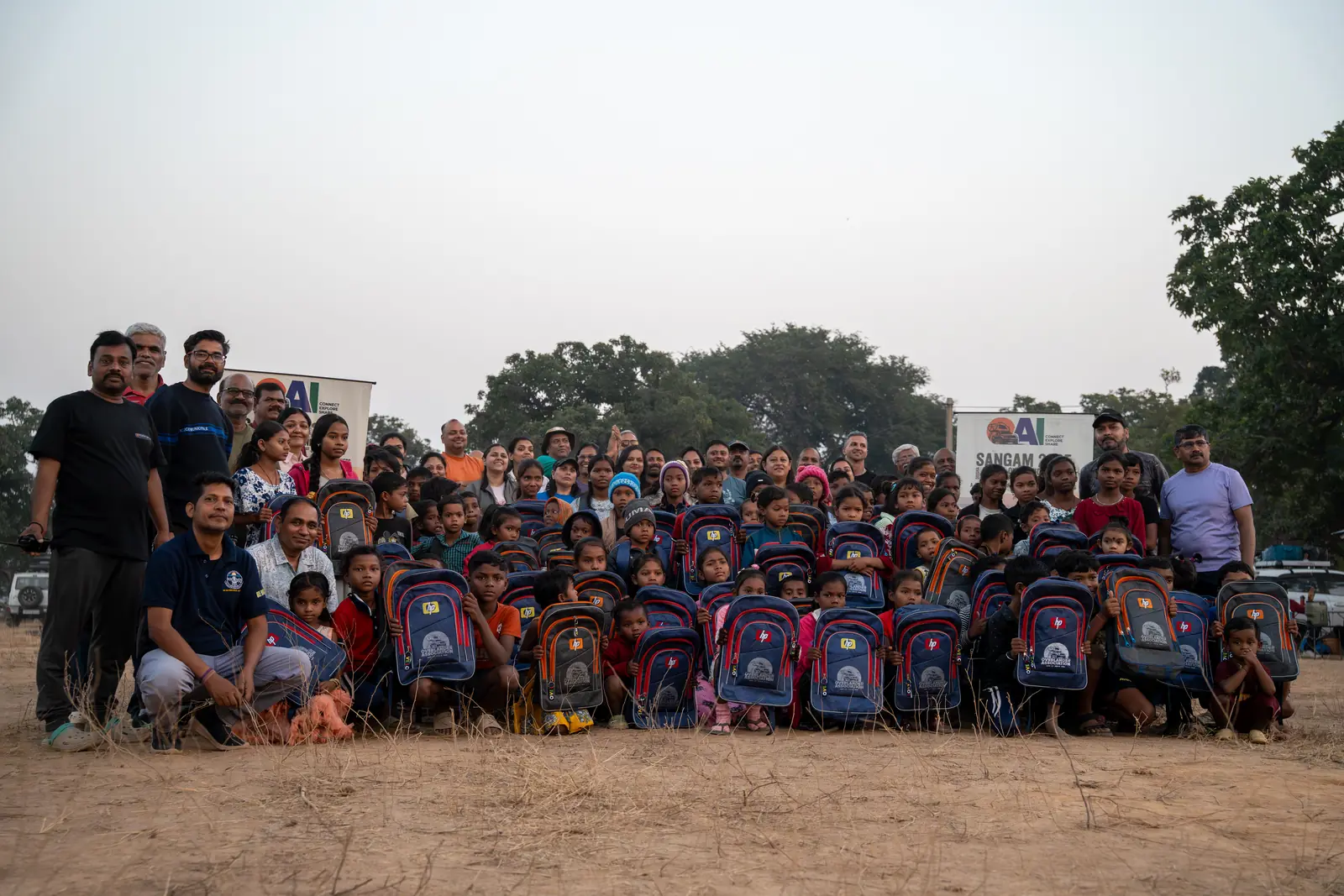 OAI members and children posing with donated school bags at a distribution drive