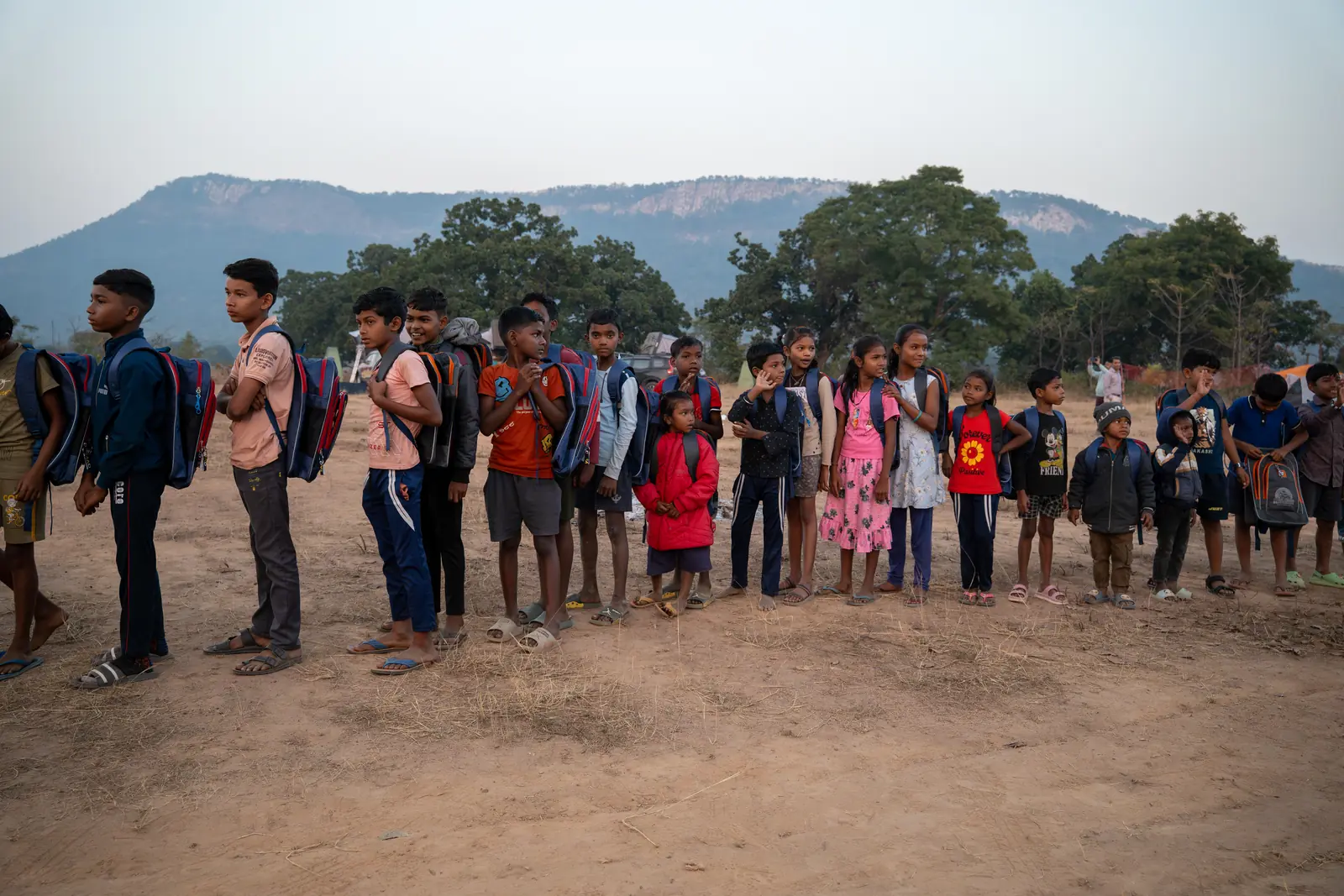 A line of schoolchildren with their new OAI-donated backpacks against a mountain backdrop