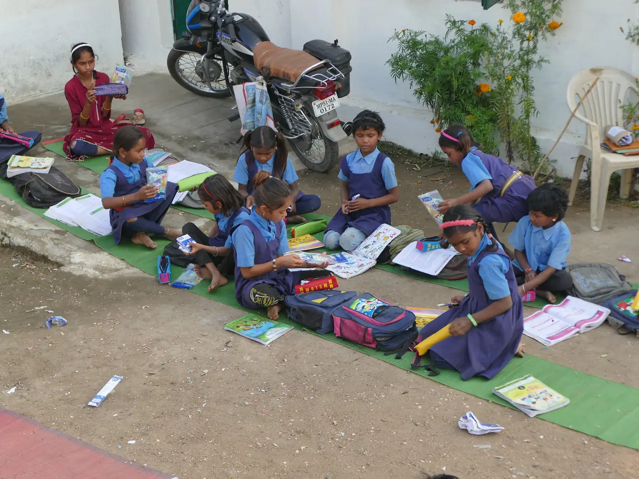 Schoolchildren unpacking their new stationery kits on mats outside their school