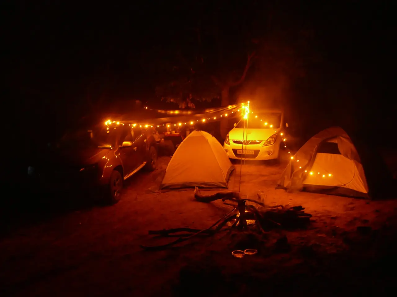 A campfire lit up at night beside tents and vehicles, Theralu Village