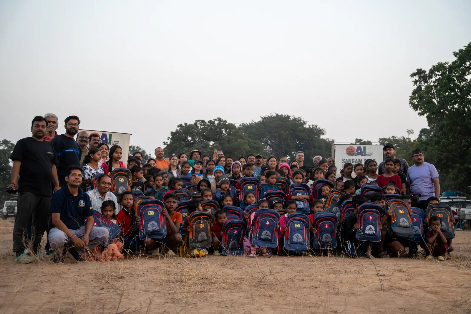 OAI members and local schoolchildren posing with donated backpacks at the Sangam 2025 grounds
